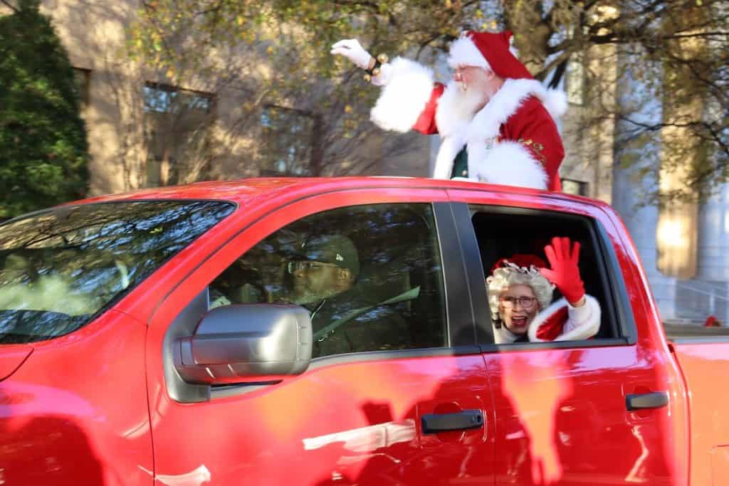 Santa and Mrs. Claus riding in a red car, waving