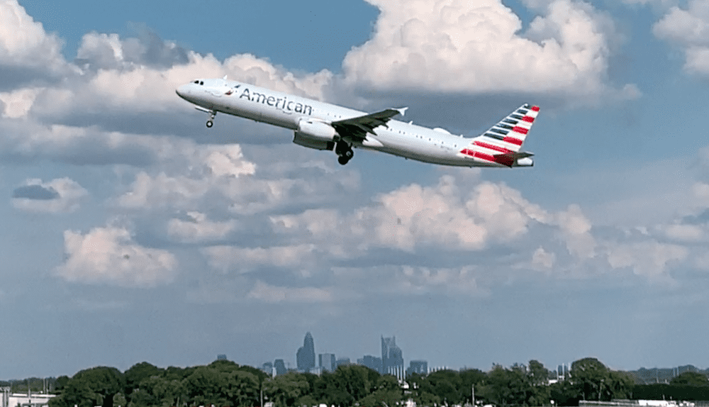 Airplane with American logo taking off from airport, with the Charlotte skyline in background