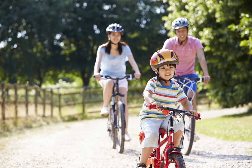 Small boy riding a red bike on a trail, followed by two adults.