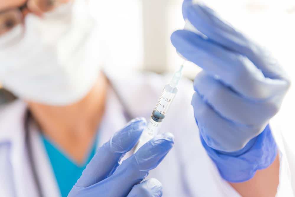 Female healthcare provider with a stethoscope on shoulder holding syringe and vaccine.