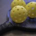 3 yellow pickleballs on a pickleball paddle
