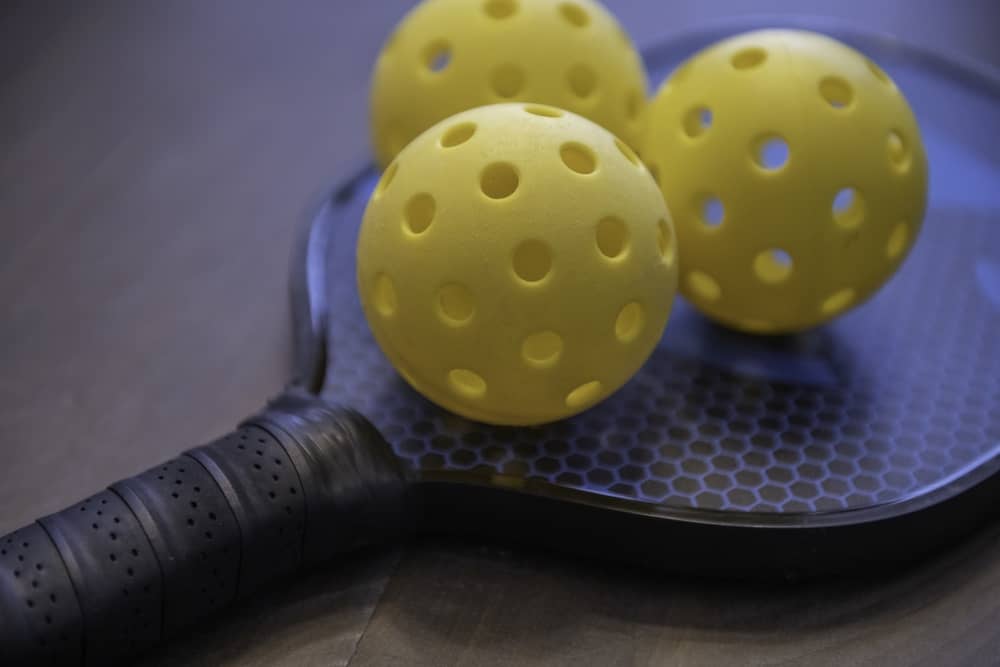 3 yellow pickleballs on a pickleball paddle
