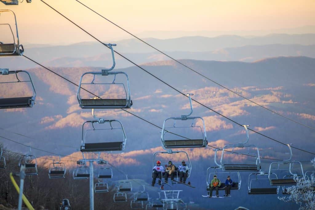 Ski lift on Beech Mountain with two carts of skiiers. Golden mountainscape in background with clear sky.