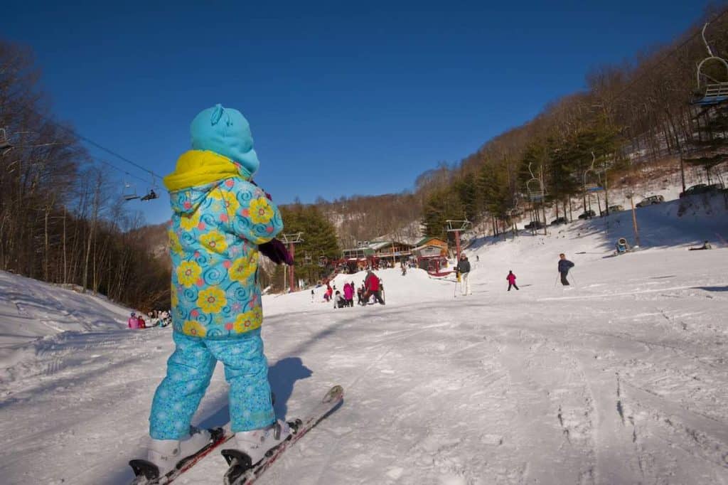 Child dressed in blue wearing skis on top of hill
