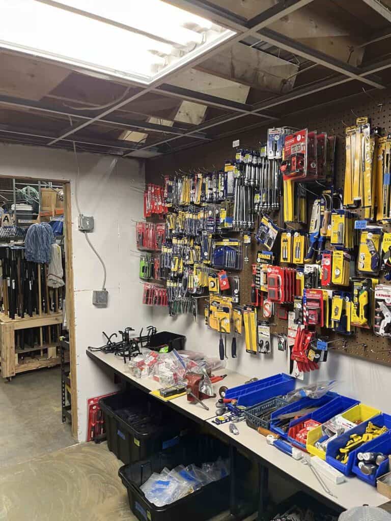 New, packaged tools hanging on pegboard display for sale. Tools on table for sale. Mops for sale.