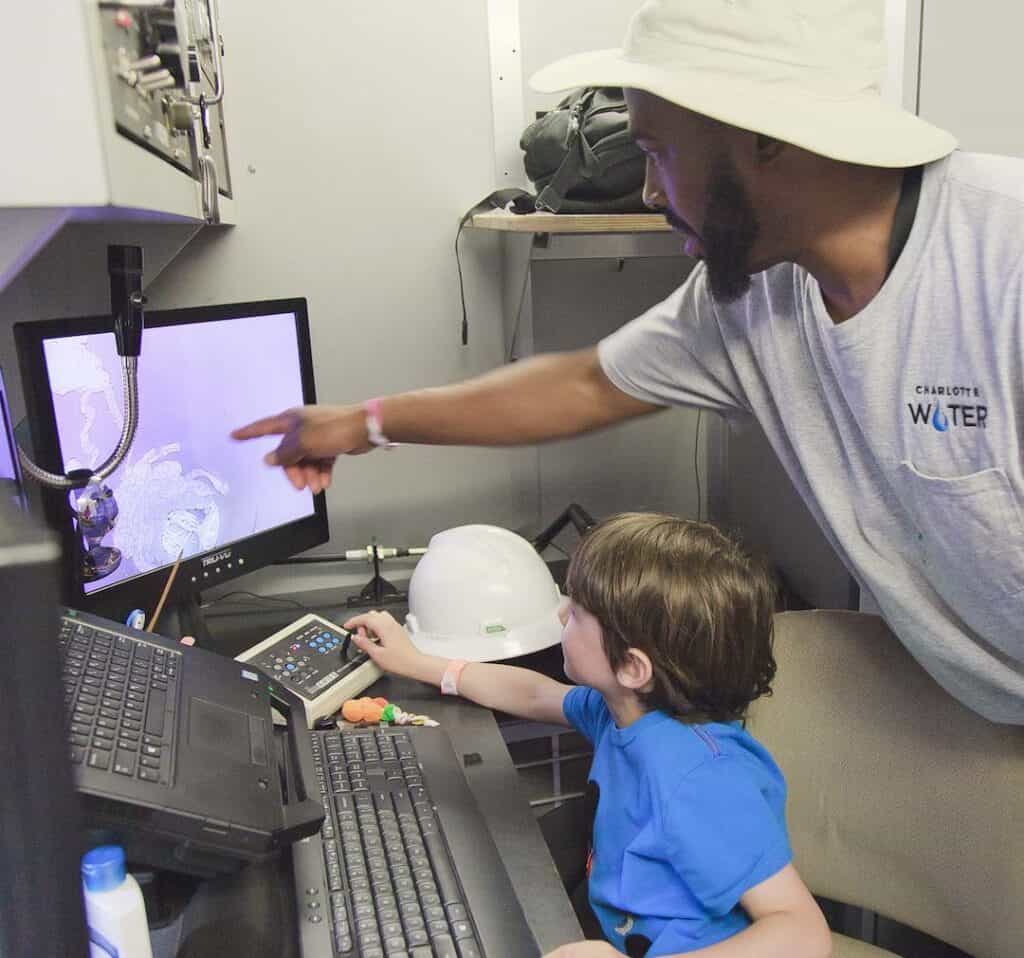 Man with Charlotte Water logo on shirt pointing to computer screen while boy looks at screen