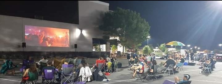 group of people in a parking lot watching a movie projected on the outside of a building