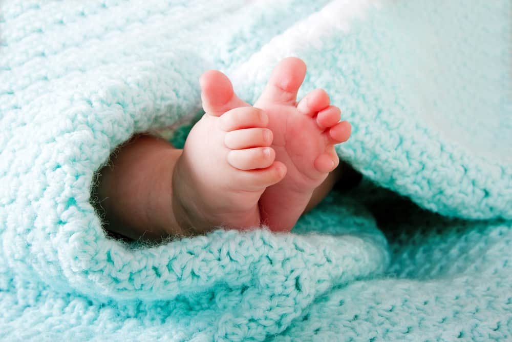 infant's feet poking out from under a light green blanket