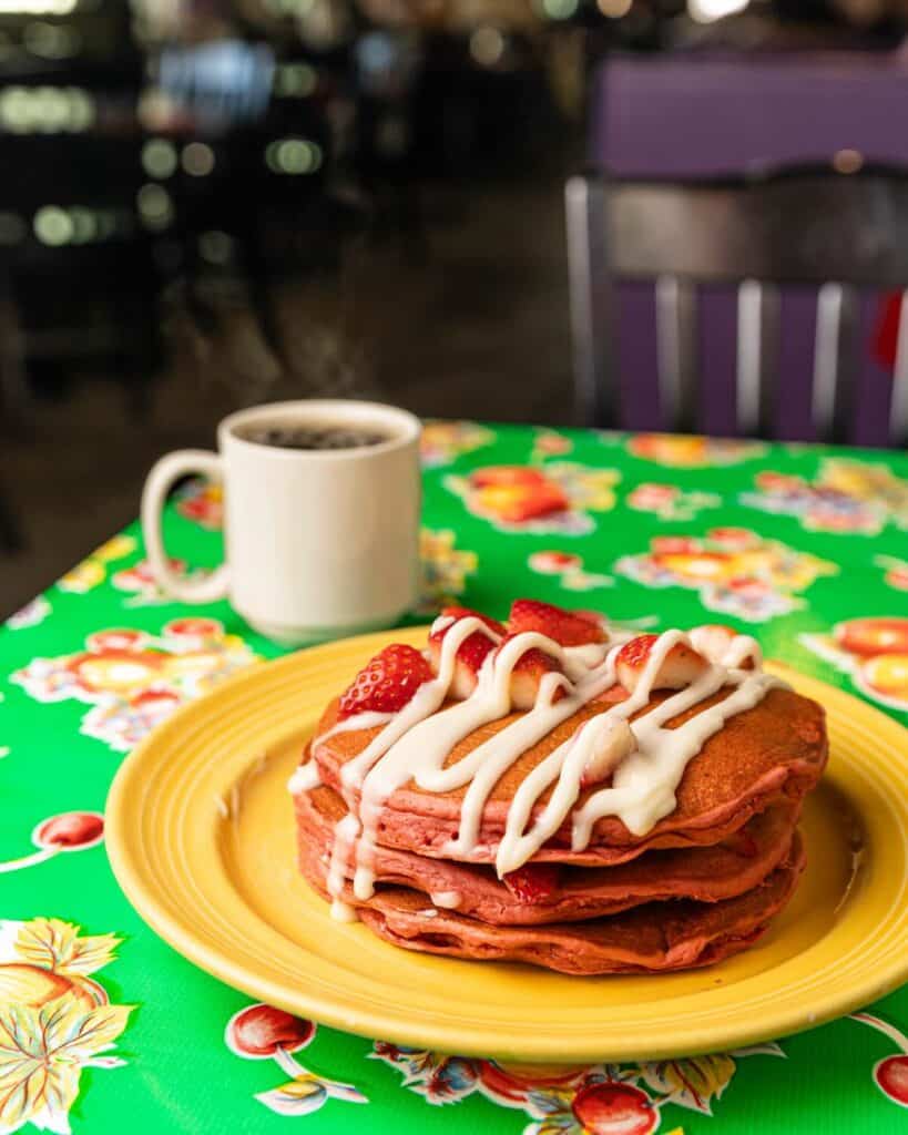 Pink pancakes on a yellow plate, with a cup of coffee