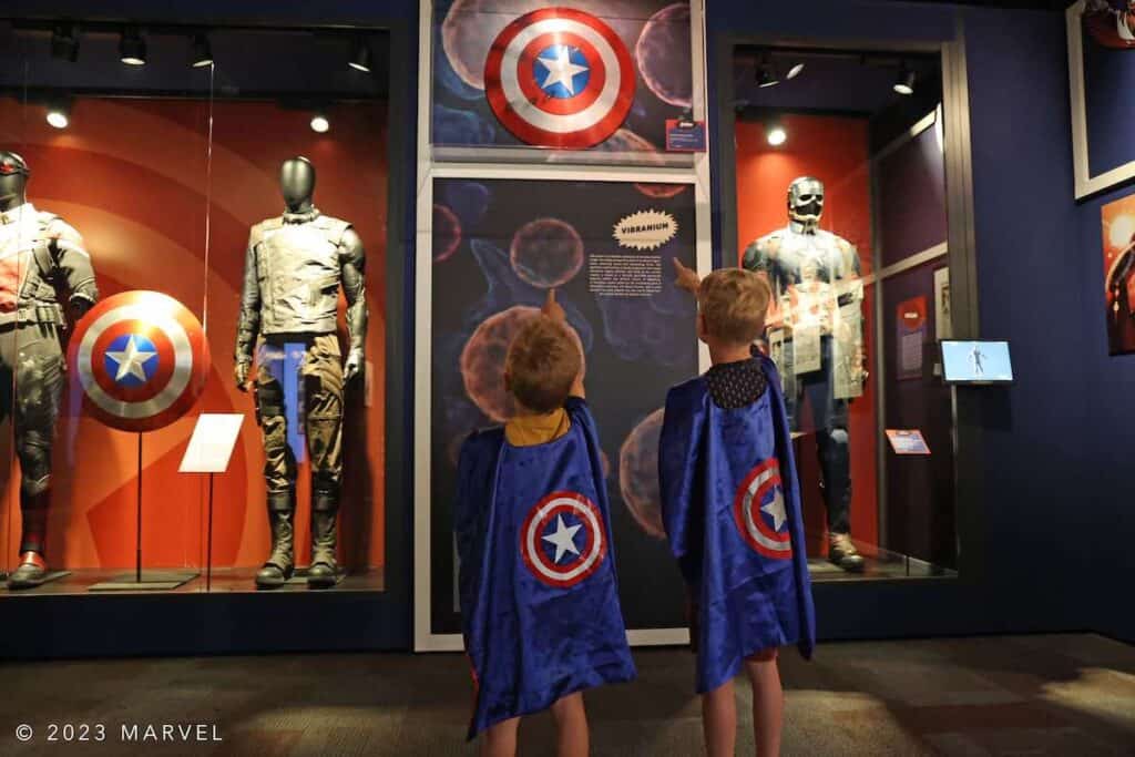 boys in capes pointing to shield at Marvel exhibit