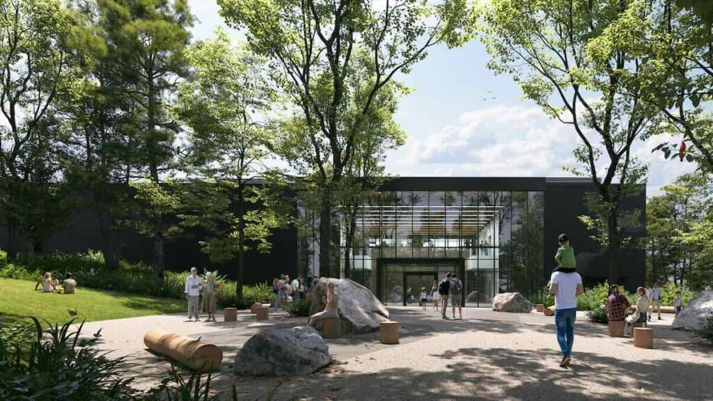Outdoor plaza with grass and rocks and a walkway. View of museum through glass windows.