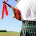 Closeup picture of male playing bagpipe on green summer outdoors background