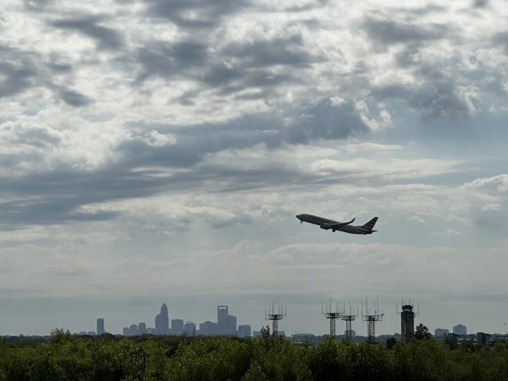 Plane taking off against backdrop of the Charlotte skyline, from the vantage point of CLT Airport Overlook