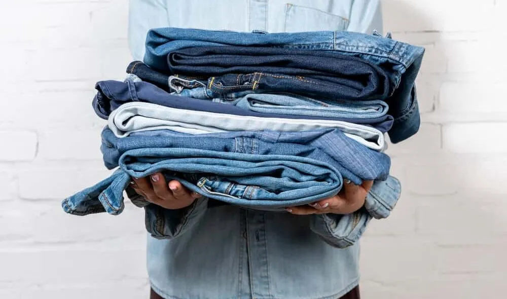 person wearing denim holding pile of jeans