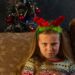 Serious little girl in red deer horns grimacing looking in camera at home face portrait. Offended angry toothless child in New Year eve Christmas tree lights. Family holidays celebration concept.