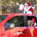 Santa and Mrs. Claus riding in a red car, waving
