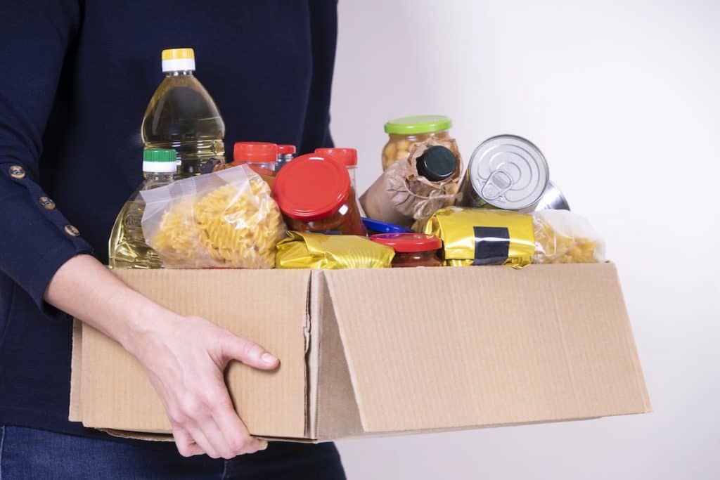 Woman volunteer hands holding food donations box with food grocery products.