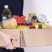 Woman volunteer hands holding food donations box with food grocery products.