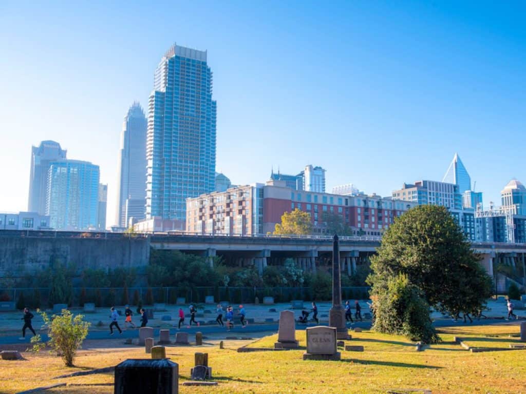 people running on path in cemetery with Charlotte city skyline in background
