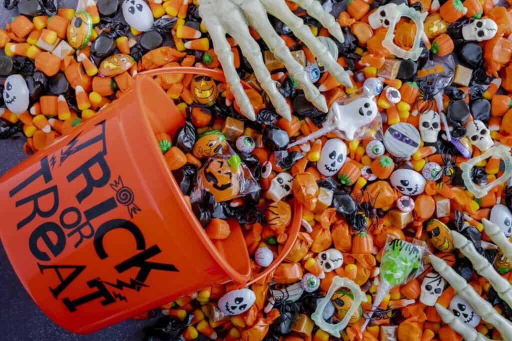 Close up of orange trick or treat pail spilling Halloween candy on black stone surface