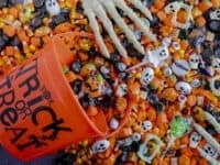 Close up of orange trick or treat pail spilling Halloween candy on black stone surface