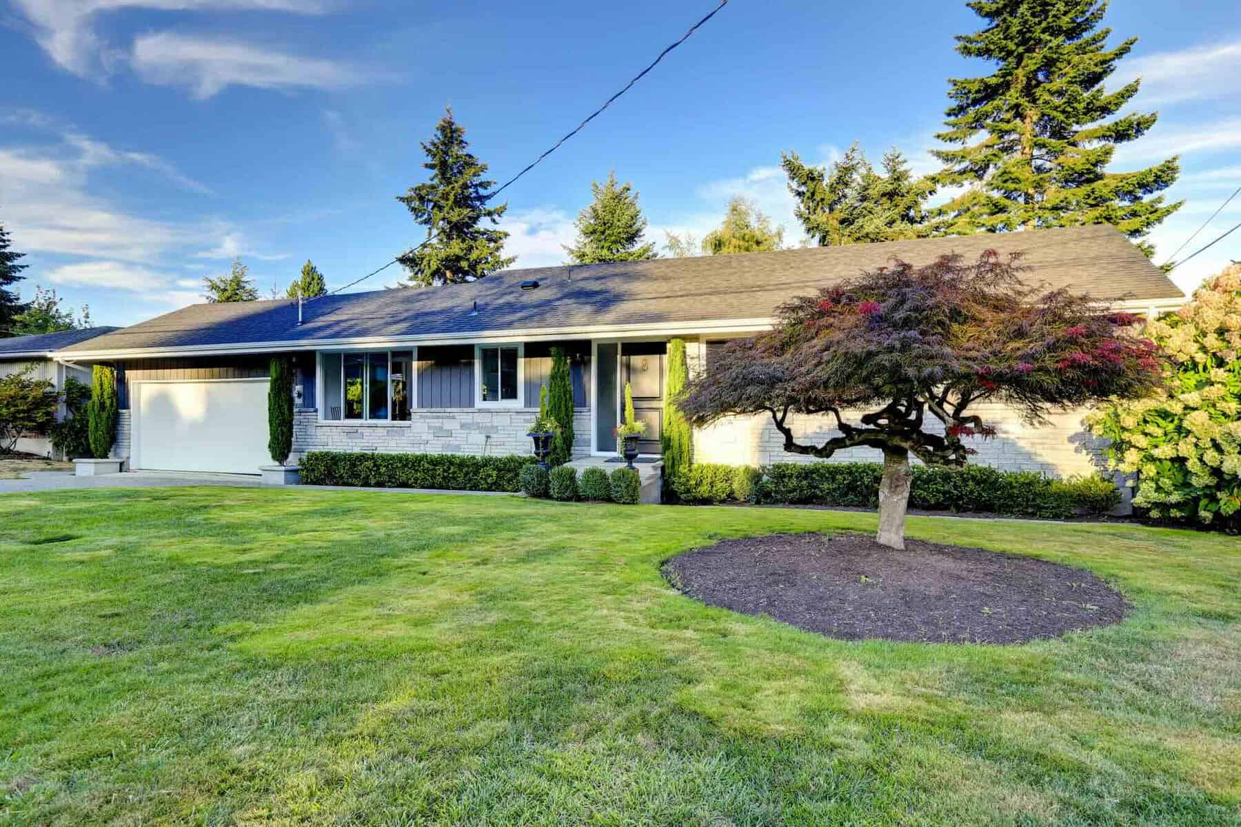 One story house with stone wall trim. View of entrance porch with front yard landscape and garage