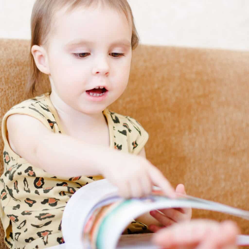 toddler sitting on couch reading book
