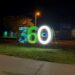 360 Sculpture. Glowing numbers 360 in blue green and white. there's an eye in the middle of the 0 and a large cane.
