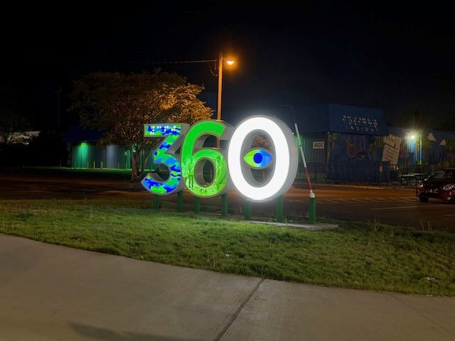 360 Sculpture. Glowing numbers 360 in blue green and white. there's an eye in the middle of the 0 and a large cane.