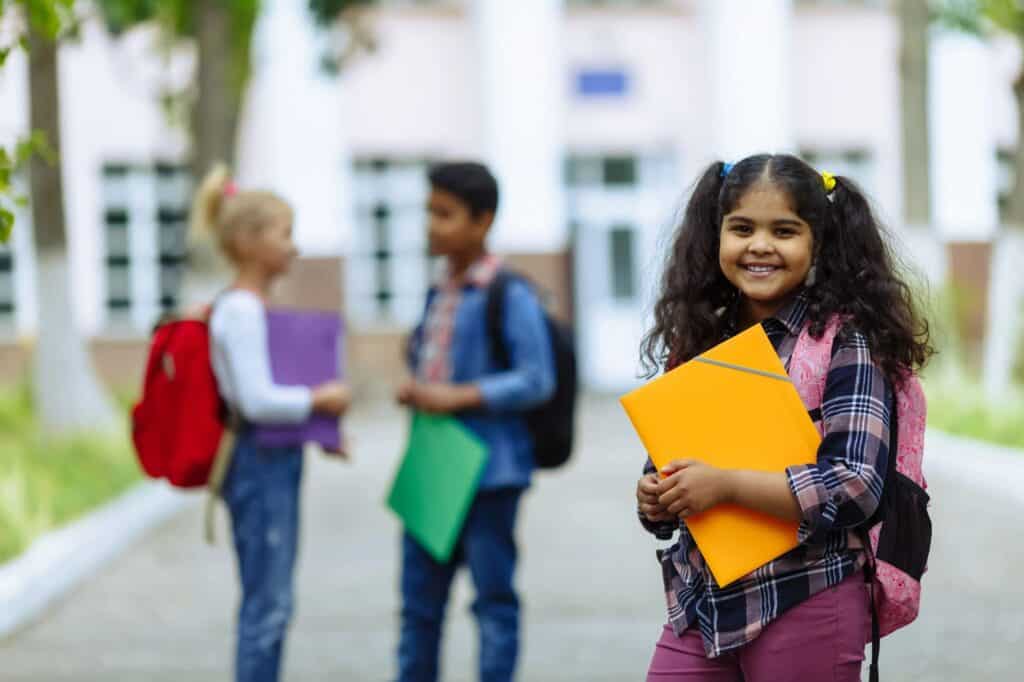 three kids holding folders in front of school